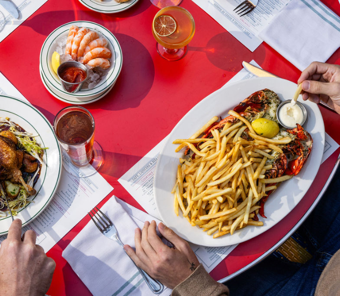 Overhead view of restaurant table with french fries, shrimp cocktail, and cocktails on red tablecloth