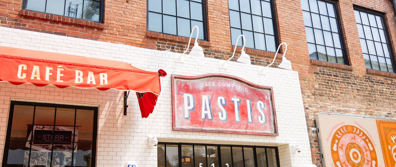 "Pastis Café Bar, brick building, red awning, signboard, cafe entrance, glass windows."